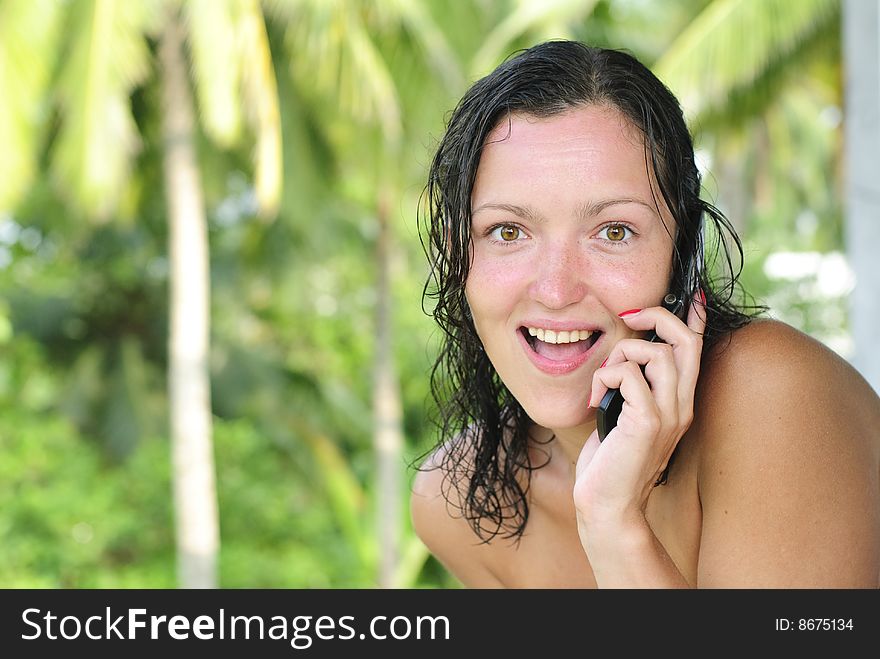 Beautiful young woman with big smile talking on the phone outdoors. Looking surprised directly at camera. Palm trees and paradise in the background. Beautiful young woman with big smile talking on the phone outdoors. Looking surprised directly at camera. Palm trees and paradise in the background.