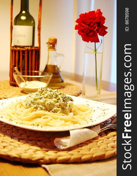 Pasta with broccoli on a white plate. Decorationn of red flower, bottle of wine and olive oil.