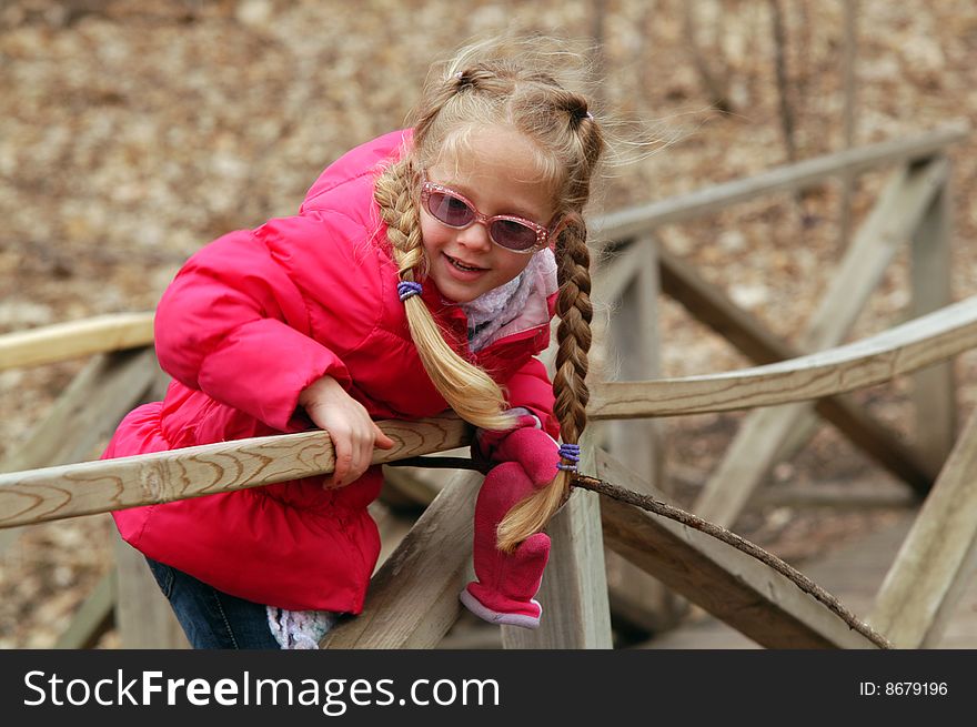 A young girl leans over the railing of a small walk bridge watching the water flow past her. She holds a stick in her hand. A young girl leans over the railing of a small walk bridge watching the water flow past her. She holds a stick in her hand.