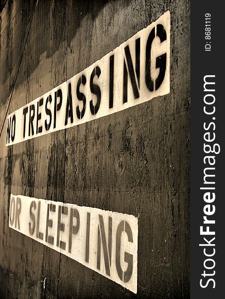 No trespassing or sleeping sign painting in black and white over grainy wooden boards