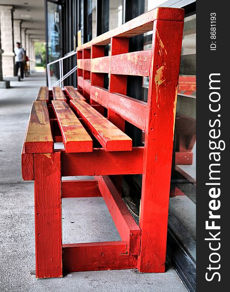 Red Bench in perspective with grainy painted wood and people in backgroun