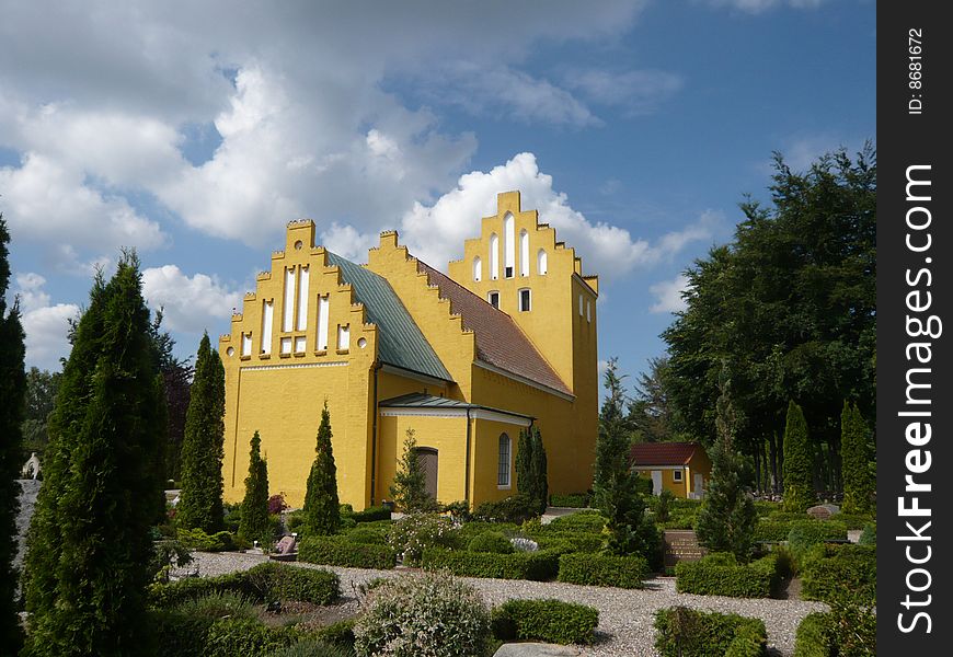 Yellow danish christian church with clouds matching the tower