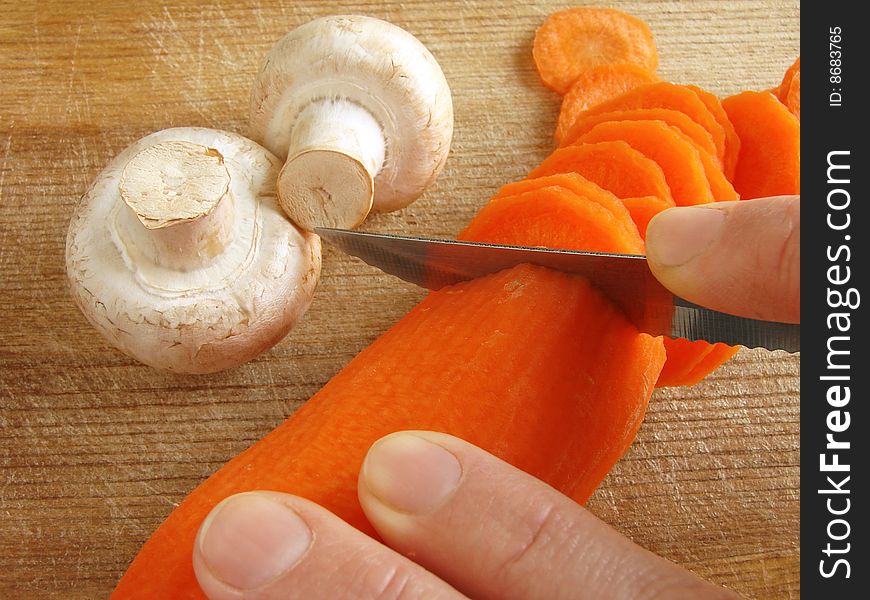 Hands cut carrot on the kitchen board with some mushrooms. Hands cut carrot on the kitchen board with some mushrooms