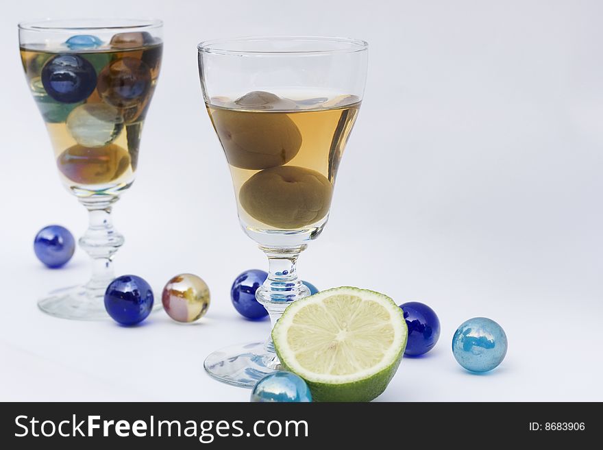 Two wine glasses filled with wine. They are filled with a Japanese wine. One glass has plums in and the other is full of marbles. There are marbles and a half of lime for decoration. Two wine glasses filled with wine. They are filled with a Japanese wine. One glass has plums in and the other is full of marbles. There are marbles and a half of lime for decoration.