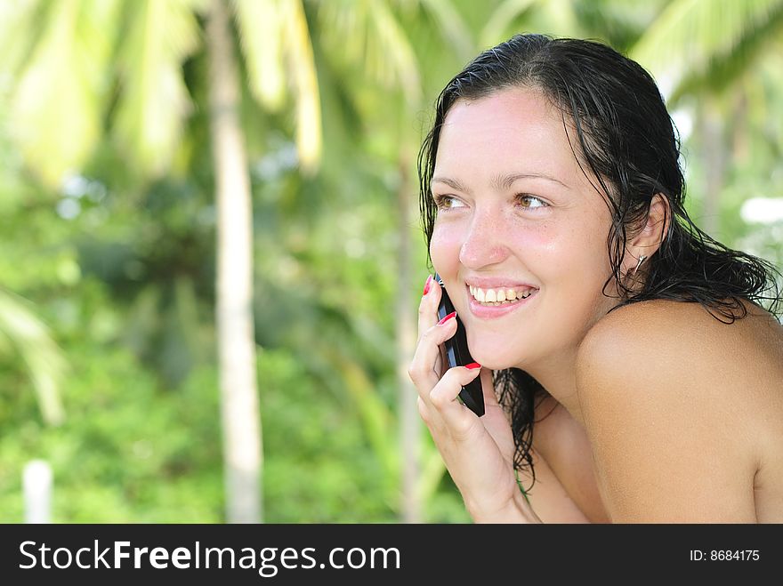 Beautiful young woman with big smile talking on the phone outdoors. Palm trees and paradise in the background. Beautiful young woman with big smile talking on the phone outdoors. Palm trees and paradise in the background.