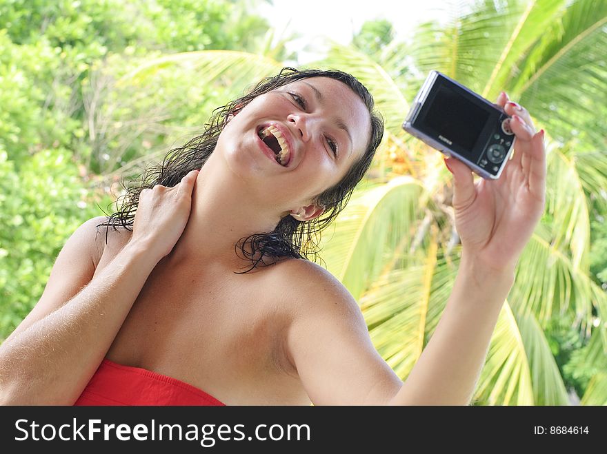 Atractive young woman taking self portrait. Vacation background with palm trees.