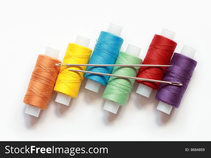 Spools of variegated thread with needles lying on white background. Spools of variegated thread with needles lying on white background