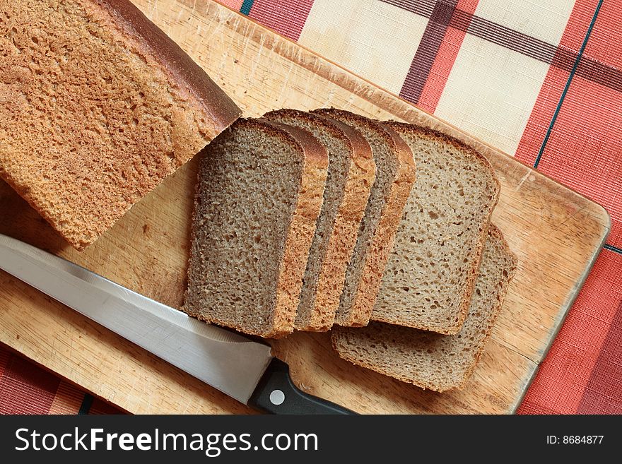 Slices of rye-bread with kitchen knife lying on breadboard. Slices of rye-bread with kitchen knife lying on breadboard