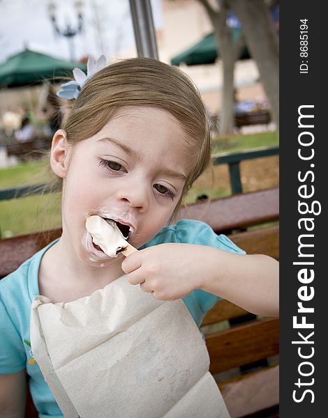 A cute little girl eats her ice cream treat at the park and gets a bit messy in the process. A cute little girl eats her ice cream treat at the park and gets a bit messy in the process