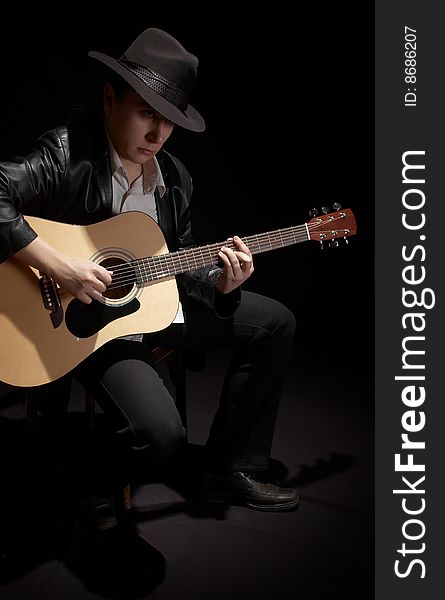 The man in a black hat plays a guitar. The man in a black hat plays a guitar