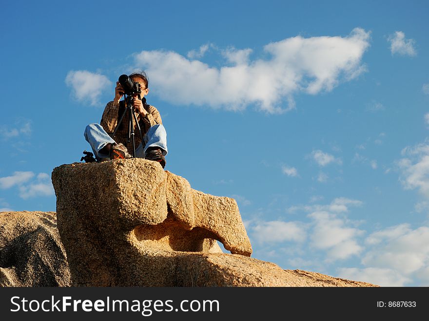 Photographer seated on a Big Rock against blue Sky. Photographer seated on a Big Rock against blue Sky