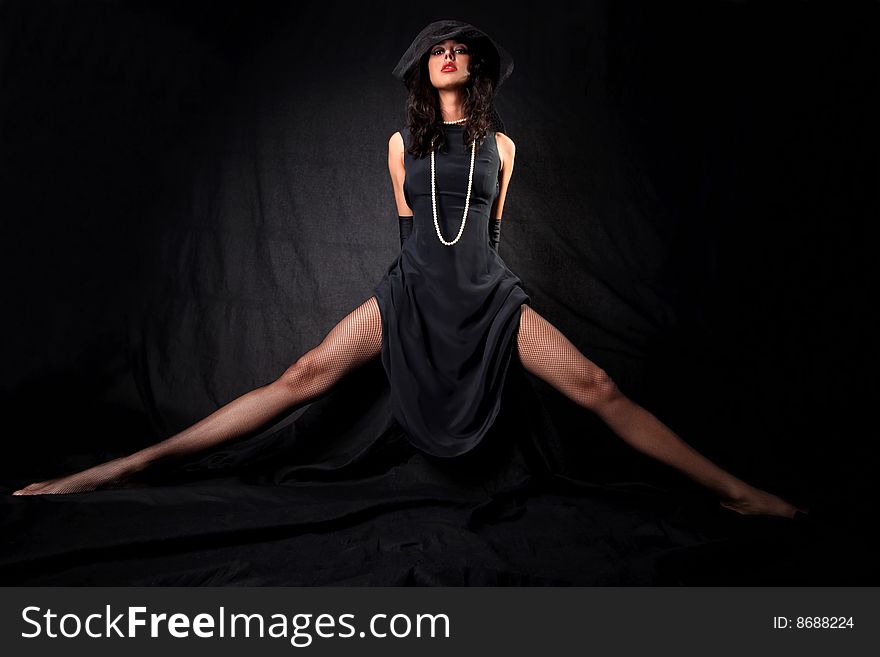 Girl with long legs in hat with veil and perl against black background