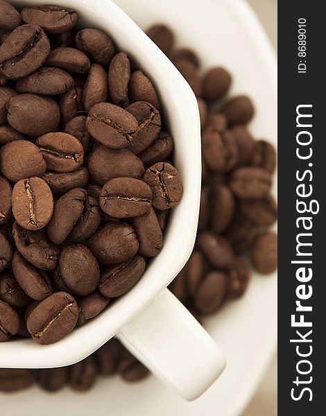 Coffee cup filled with coffee beans, and coffee beans scattered over a plate. Coffee cup filled with coffee beans, and coffee beans scattered over a plate