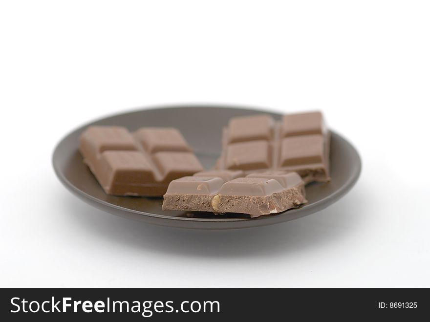 Dark chocolate pieces with brown saucer on white background. Selective focus. Dark chocolate pieces with brown saucer on white background. Selective focus