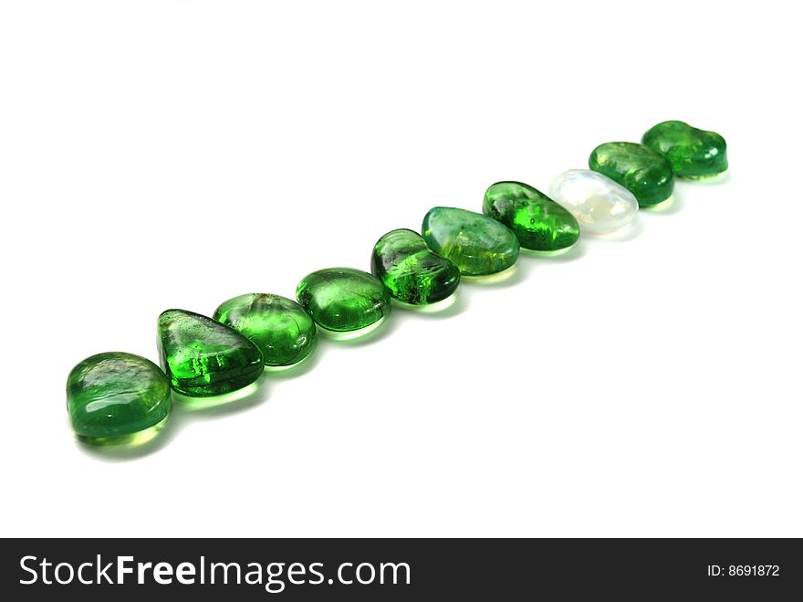 A number of green stones and one white on white background. A number of green stones and one white on white background