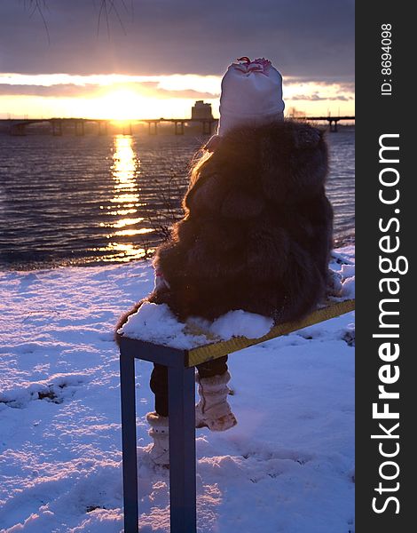 Little girl sitting on bench look at winter sunset. Little girl sitting on bench look at winter sunset