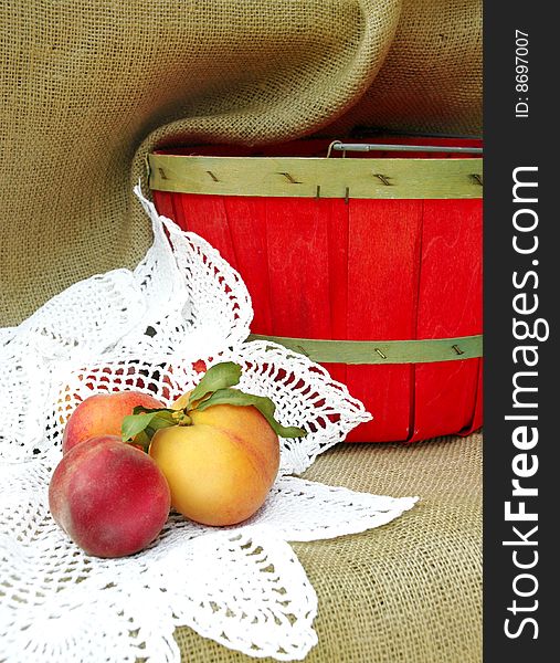 A still life with three peaches on a crocheted white doily next to a red basket, vertical with copy space. A still life with three peaches on a crocheted white doily next to a red basket, vertical with copy space