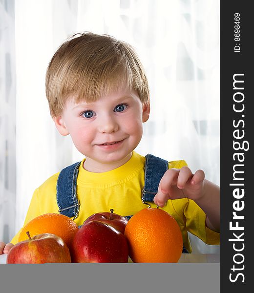 The child sits on a table with fruit. The child sits on a table with fruit