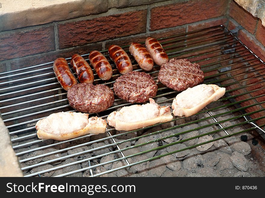 Sausages, burgers, and pork chops cooking on a barbecue. Sausages, burgers, and pork chops cooking on a barbecue.