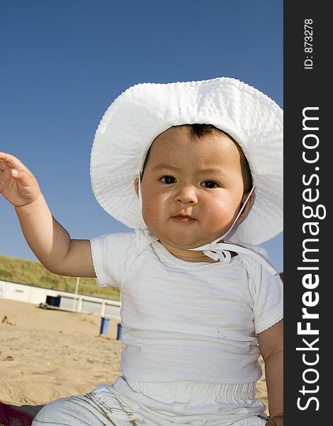 Lovely baby girl waving at the beach, wearing a hat. Lovely baby girl waving at the beach, wearing a hat