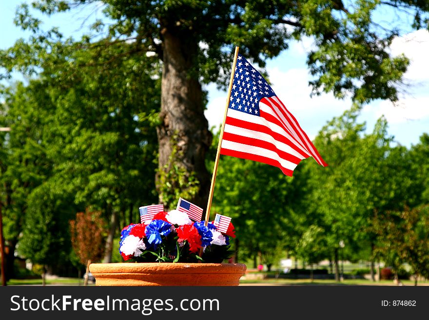 Red, white and blue carnation decoration with American flags in front of a large shade tree. Red, white and blue carnation decoration with American flags in front of a large shade tree