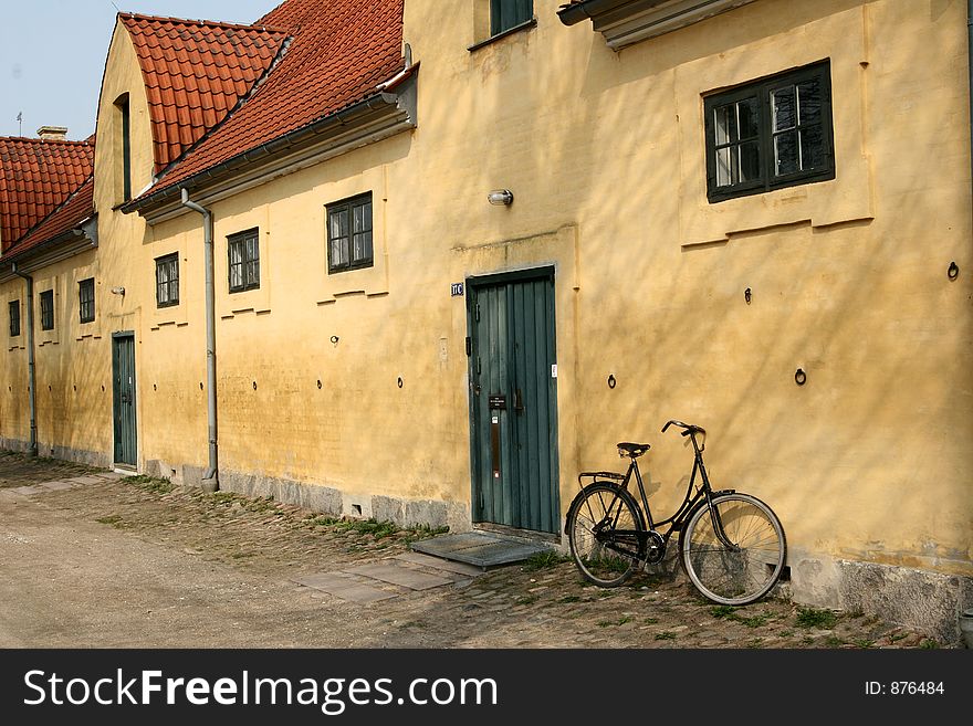 Large yellow l house   a sunny summer day with a bike  in a village in denmark. Large yellow l house   a sunny summer day with a bike  in a village in denmark