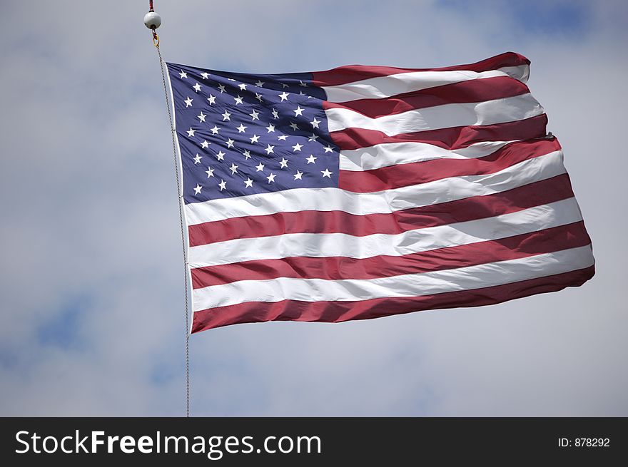 A large United States flag waves in the wind as it is suspended from a crane at a veteran's flag memorial event. A large United States flag waves in the wind as it is suspended from a crane at a veteran's flag memorial event.