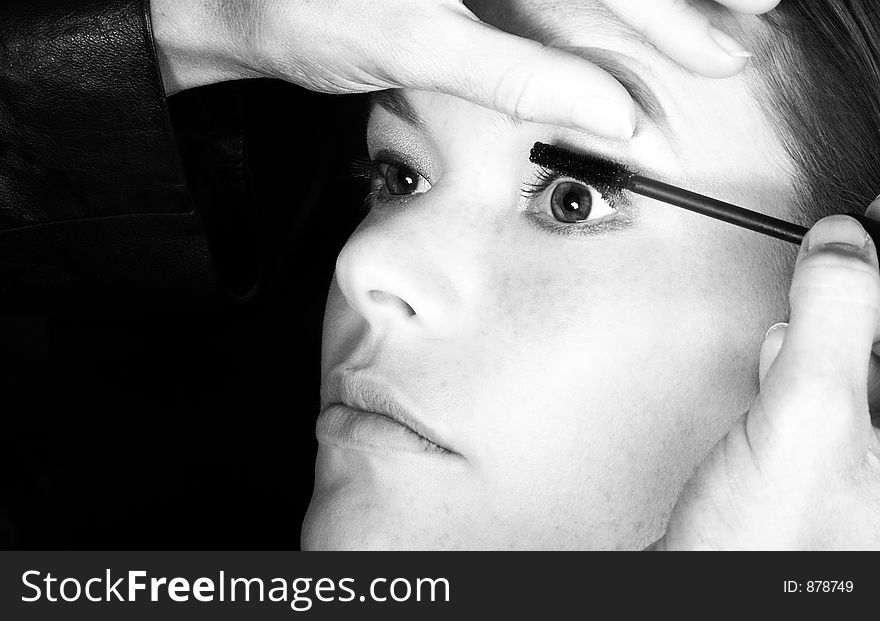 Make-up artist applying mascara to young woman?s lashes - black and white