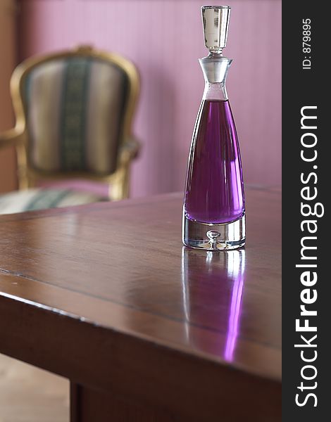Crystal decanter with purple liquore on top of a wooden table. A classic french chair is seen in the background.