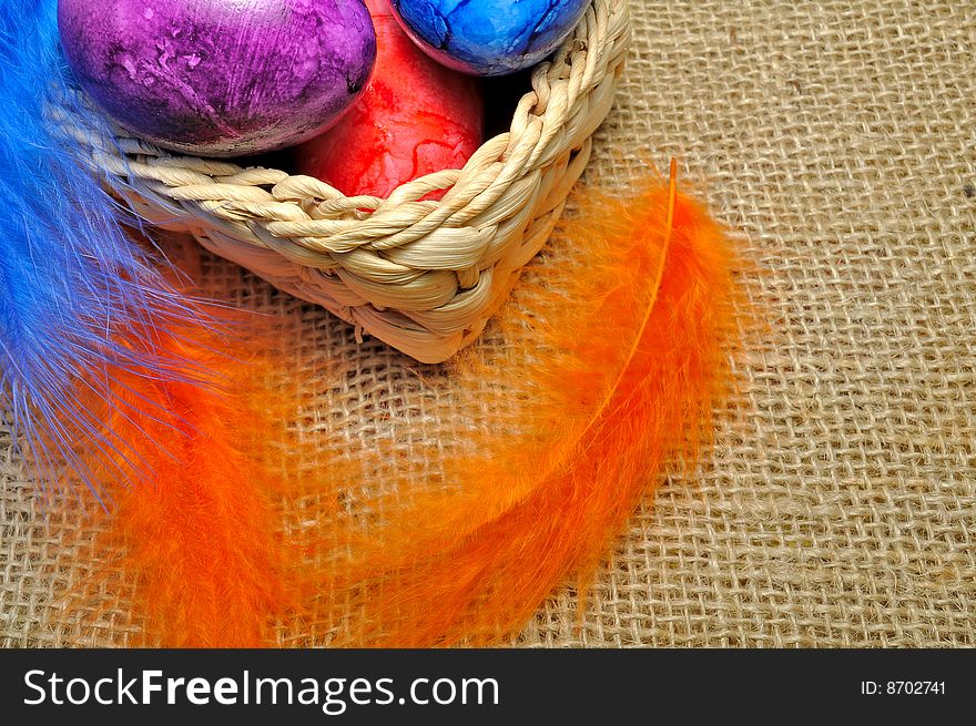 Colorful Easter eggs in basket with feathers hanging around.