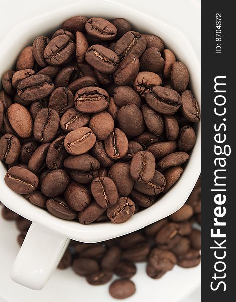 Coffee cup filled with coffee beans, and coffee beans scattered over a plate. Coffee cup filled with coffee beans, and coffee beans scattered over a plate