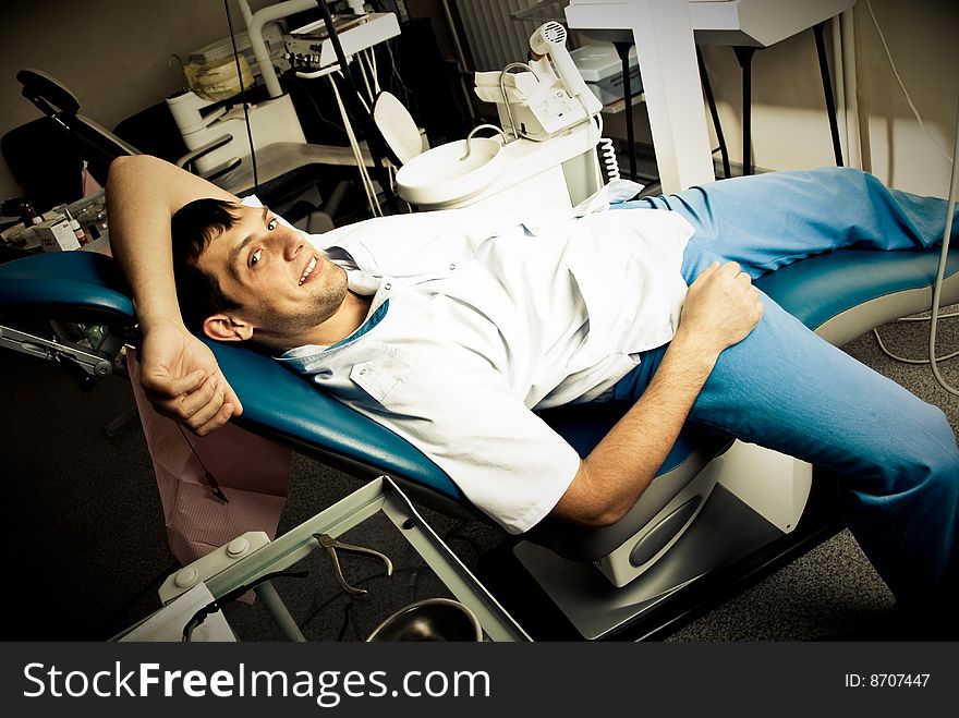Young man (a dentist or a patient) lies on the chair in the dentist's office in a very relaxed pose ans smiles. Young man (a dentist or a patient) lies on the chair in the dentist's office in a very relaxed pose ans smiles
