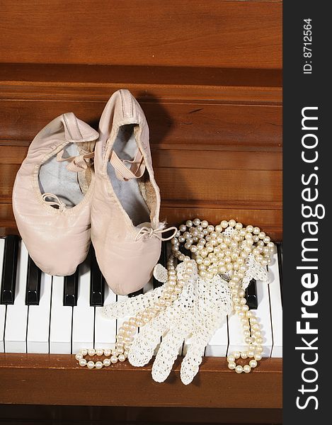 Ballet shoes, lace glove and pearls on a piano keys