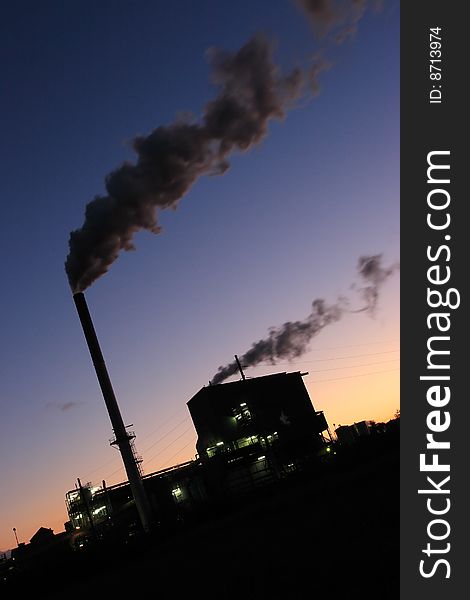 A sugar mill and steaming smoke stacks set against a colorful sunset sky. A sugar mill and steaming smoke stacks set against a colorful sunset sky.