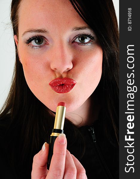 Female model applying lipstick to her lip then pullinga facial expression that seems to be blowing a kiss or pouting
