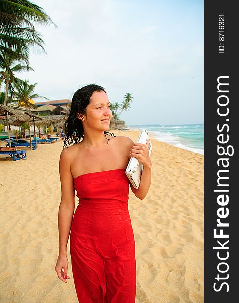 Beautiful young woman walking with laptop on the beach. The sun is setting and light is moody, sheï¿½s smiling and content after good days work. Beautiful young woman walking with laptop on the beach. The sun is setting and light is moody, sheï¿½s smiling and content after good days work.