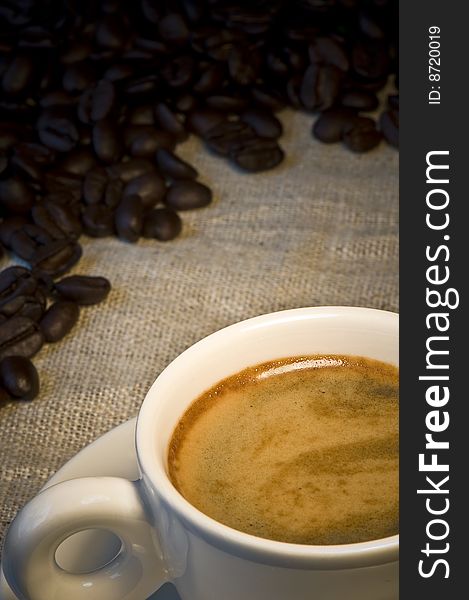 Closeup of a small white cup of freshly brewed coffee with coffee beans in background