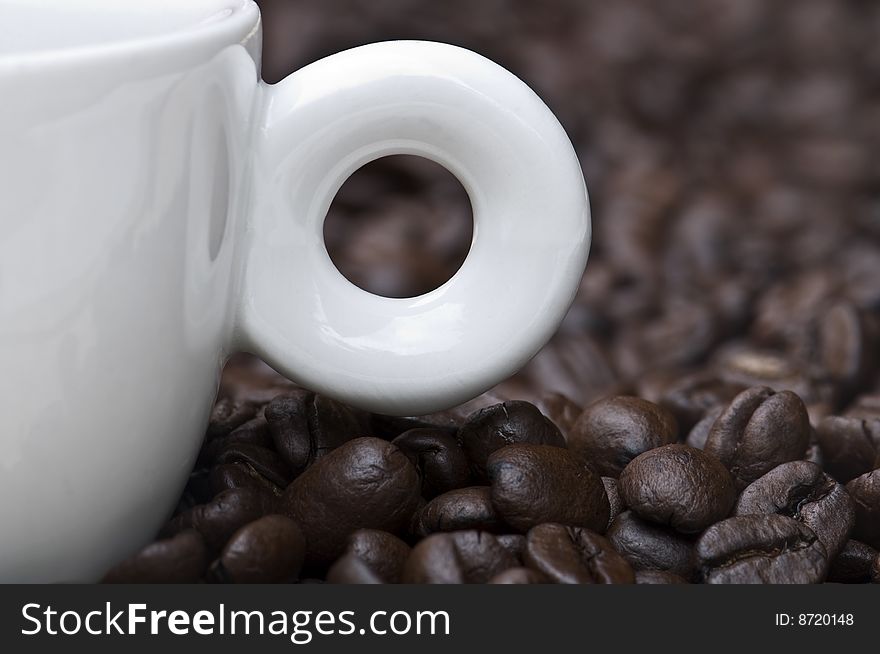 Closeup of a small white cup of freshly brewed coffee with coffee beans in background