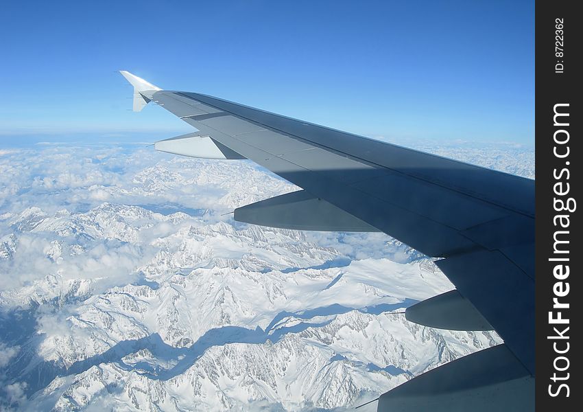 Flying over the Alps - view of airplane wing over snow capped mountains