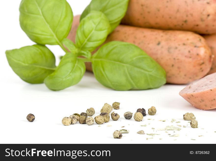 Detail of sausages with basil and green pepper on a white background