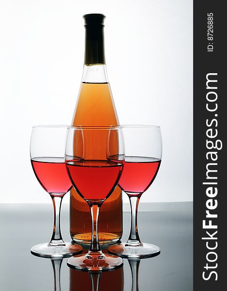 Bottle and glasses of wine on white background with reflections