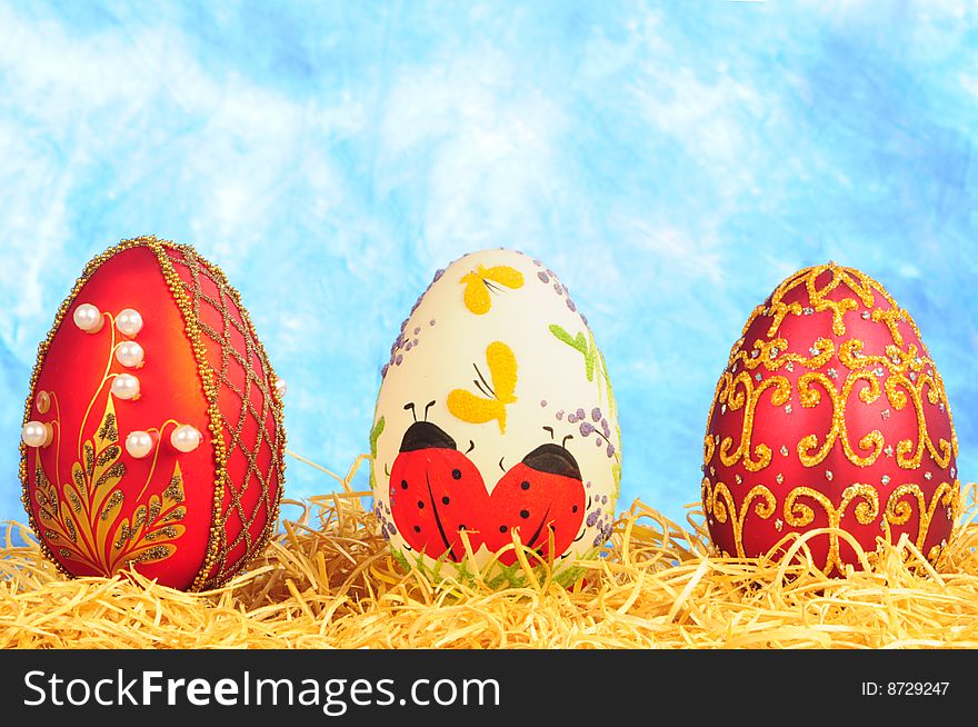 Three luxury easter eggs in straw on blue background