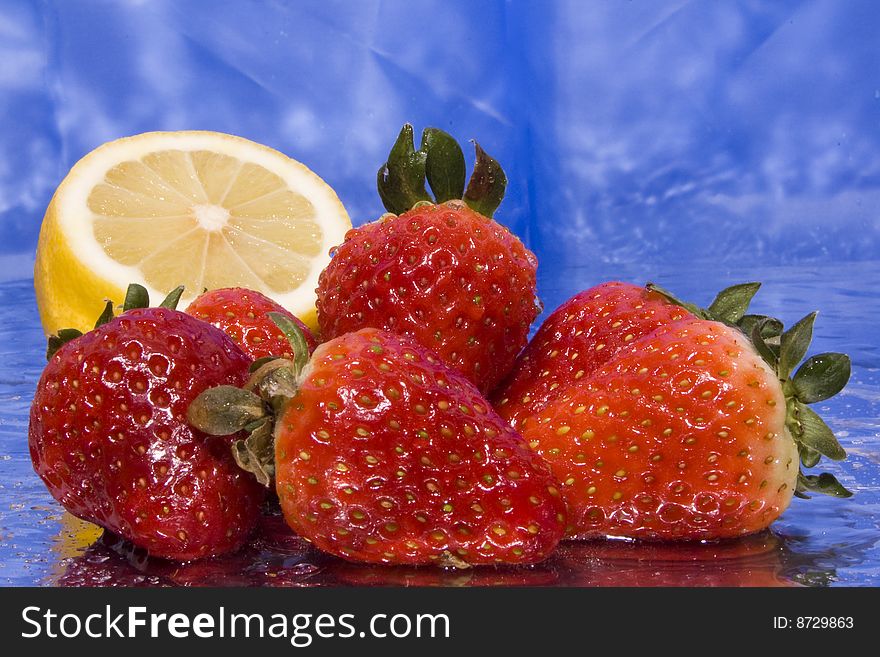 Several wet strawberries and lemon with blue background