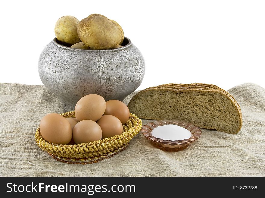 Still-life from vegetarian food. Fresh eggs lying in a wattled small basket, fragrant rye bread, a boiled potato in a pig-iron kettle, a saltcellar on a rough fabric