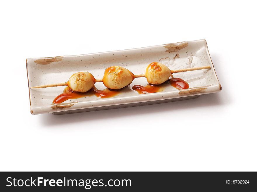 Eggs yolk roasted on skewer with sauce in white squared plate over white background
