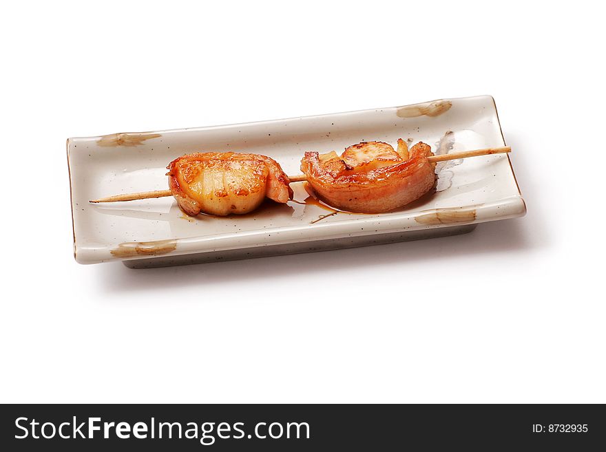 Meat and lard roasted on skewer with sauce in white squared plate over white background