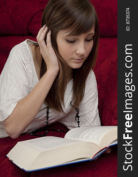 Female teenager reads book, lying on a red bench