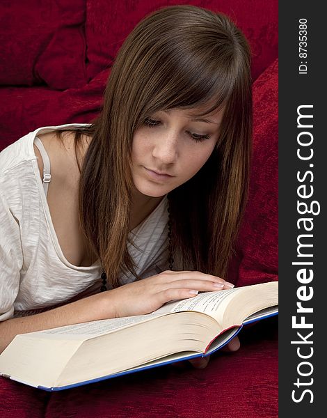 Female teenager reads book, lying on a red bench