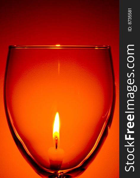 Lit candle seen through a wine glass with red background. Lit candle seen through a wine glass with red background