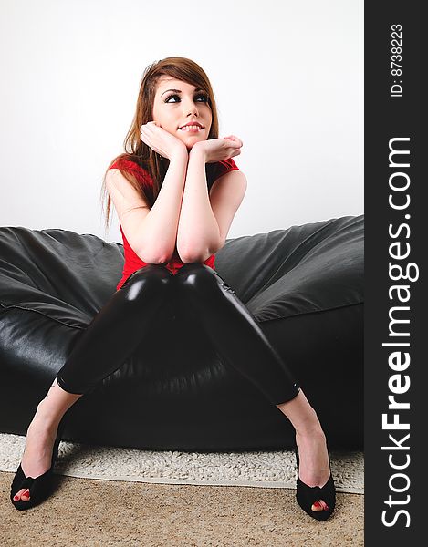 Female fashion model sitting on a leather puffy with her hands under her chin. Female fashion model sitting on a leather puffy with her hands under her chin.